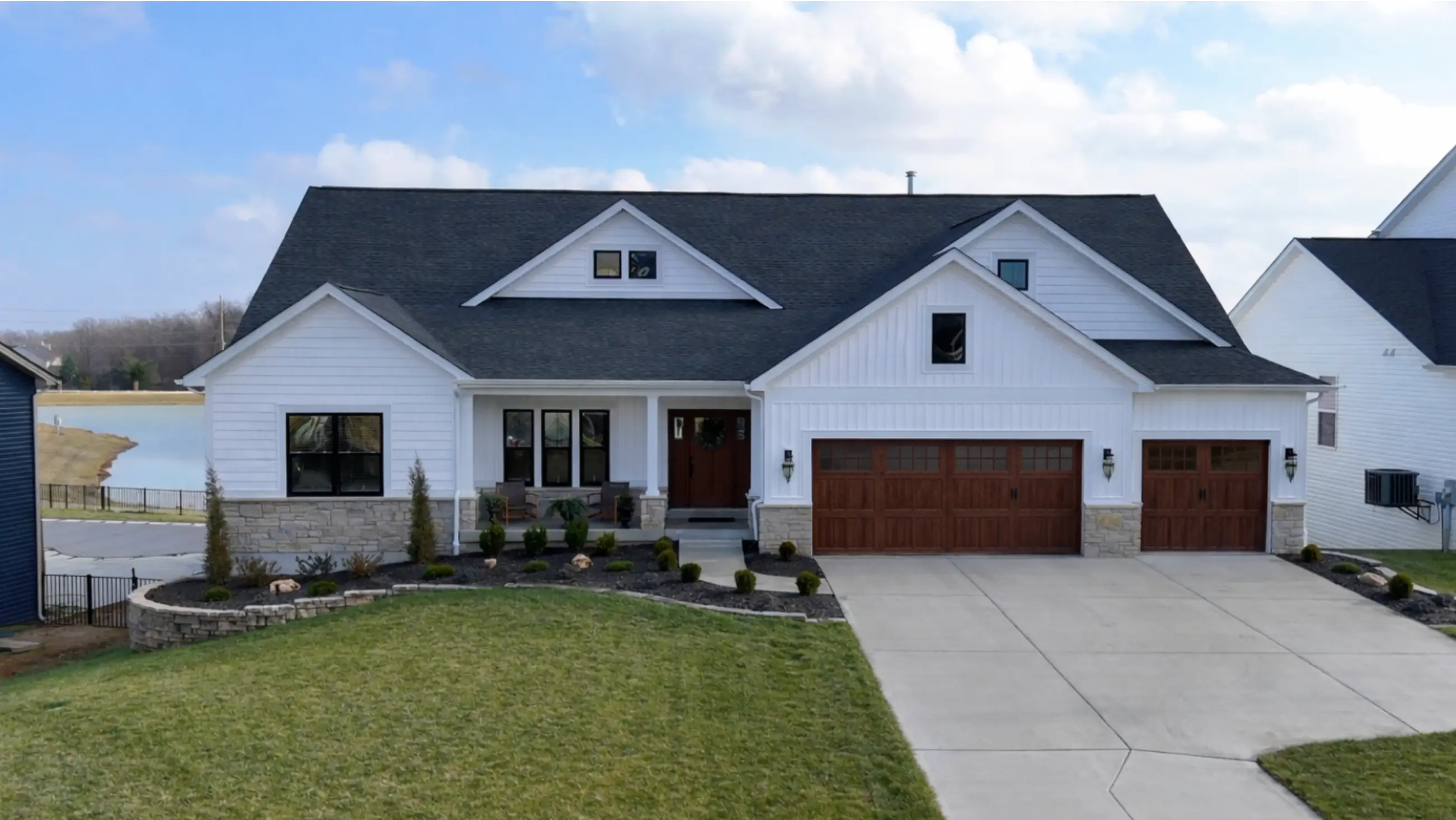 102 Royal Troon — white craftsman ranch with wood-toned garage doors overlooking a lake.